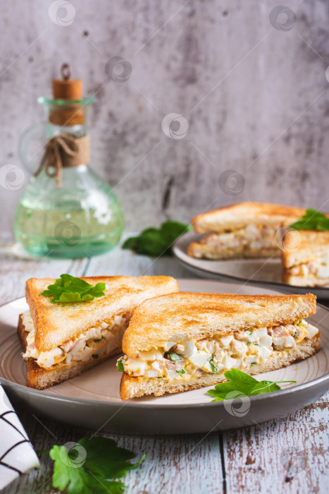 Скачать Нарезанные бутерброды с яйцом, беконом и салатом из зелени на тарелке на столе вертикальный вид фотосток Ozero