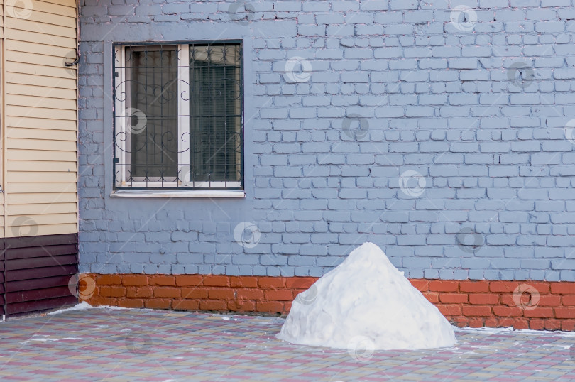 Скачать Куча снега на тротуаре рядом с кирпичным домом с зарешеченным окном. Результат работы уборщика. Улица зимнего города. Никаких людей фотосток Ozero
