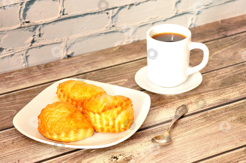 Скачать Тарелка с несколькими творожными булочками и чашкой горячего черного кофе на деревянном столе. фотосток Ozero