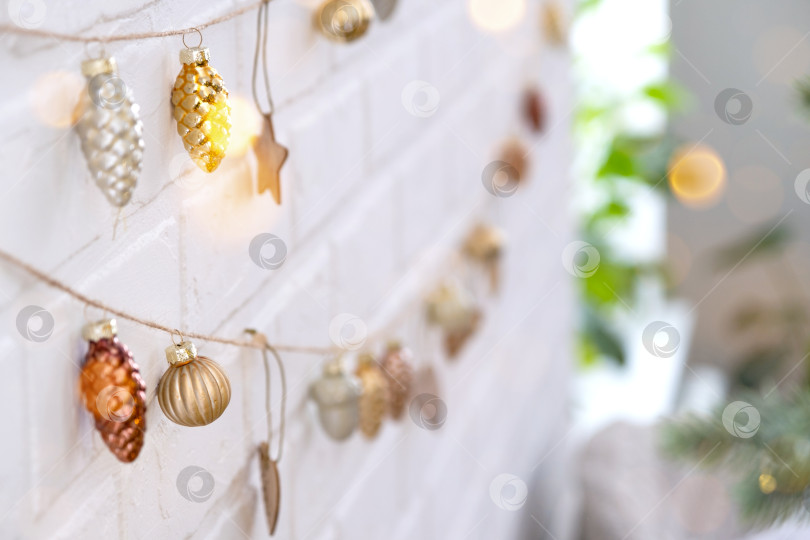 Скачать Стеклянные елочные игрушки на джутовой веревке висят на белой кирпичной стене - праздничный декор в стиле лофт, новогоднее настроение. copy space фотосток Ozero