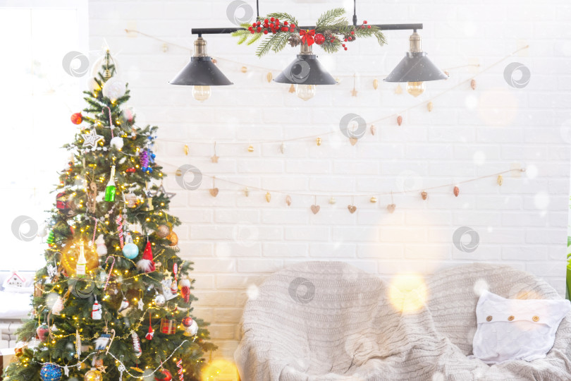 Скачать Рождественская елка в белом интерьере дома с кирпичными стенами в стиле лофт с гирляндами стеклянных игрушек на веревке. Светящиеся гирлянды украшают комнату-студию. Уютный дом на Рождество и новый год фотосток Ozero