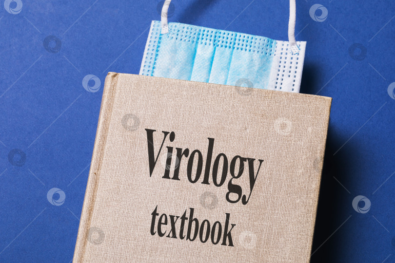 Скачать Учебник по вирусологии с закладкой из медицинской маски на столе фотосток Ozero