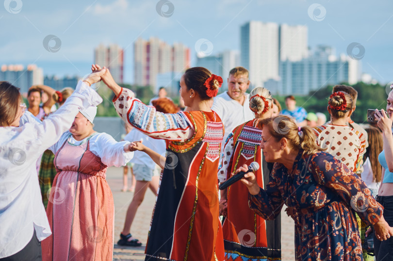 Скачать БЛАГОВЕЩЕНСК, РОССИЯ - 15 июля 2023 года: Выступление творческой группы в русских народных костюмах на набережной. Ансамбль песни и пляски танцует и поет в хороводе вместе со зрителями фотосток Ozero