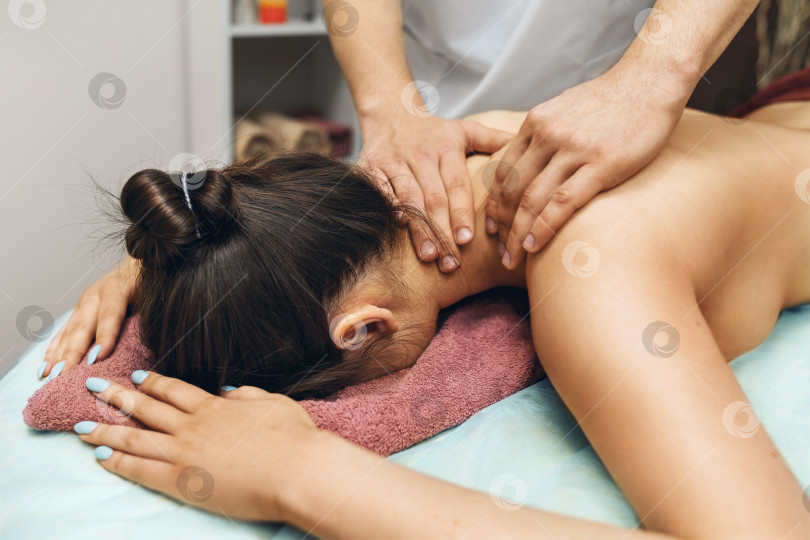 Скачать Мужчина- мануальный терапевт, делающий женщине массаж шеи и трапециевидных мышц в своем кабинете фотосток Ozero