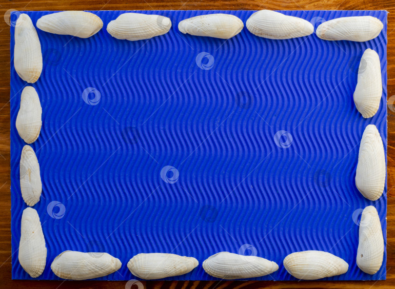 Скачать Плоский вид сверху. Текстурная композиция на деревянной поверхности представляет собой синий волнистый лист с обрамлением из белых ракушек по краям фотосток Ozero