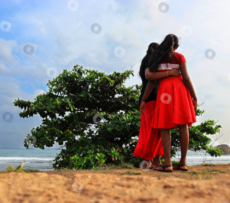 Скачать Обнимающиеся мать и дочь на берегу Индийского океана смотрят на воду. Шри-Ланка фотосток Ozero