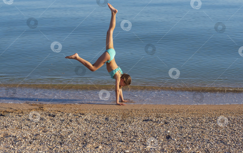 Скачать Молодая женщина делает колесо на улице. девушка, занимающаяся акробатической гимнастикой, в бикини на пляже. Молодая женщина, принимающая позу у кромки воды. С пространством для копирования фотосток Ozero