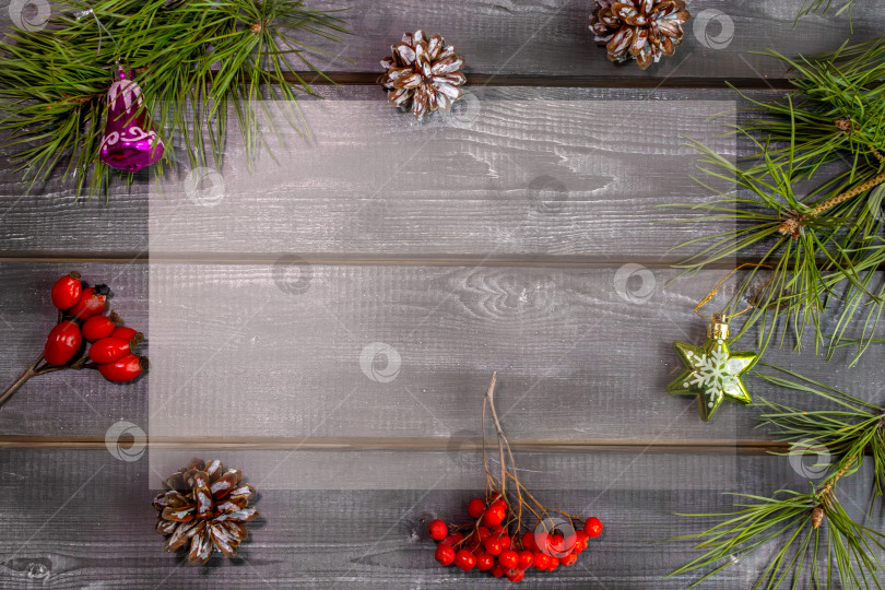 Скачать Деревянный рождественский фон с натуральными сосновыми иголками, ягодами, шишками и елочными игрушками. Рамка для надписей, поздравительной открытки фотосток Ozero