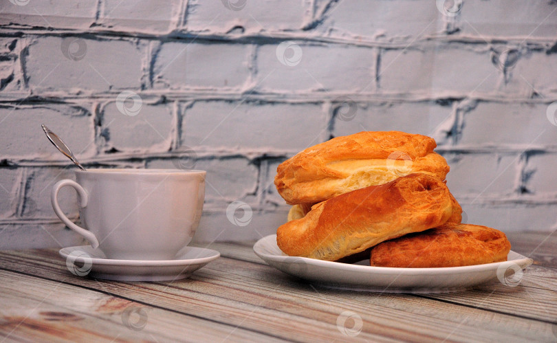 Скачать Тарелка со свежей домашней выпечкой и чашка горячего чая на блюдце на светлом деревянном столе у кирпичной стены. фотосток Ozero