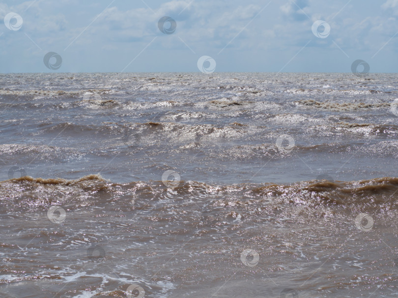 Скачать Вид на море с берега, темные волны с солнечными бликами. Пейзаж Азовского моря ветреным летним вечером. Блестящие волны на поверхности мутной воды, голубое небо с облаками, горизонт фотосток Ozero