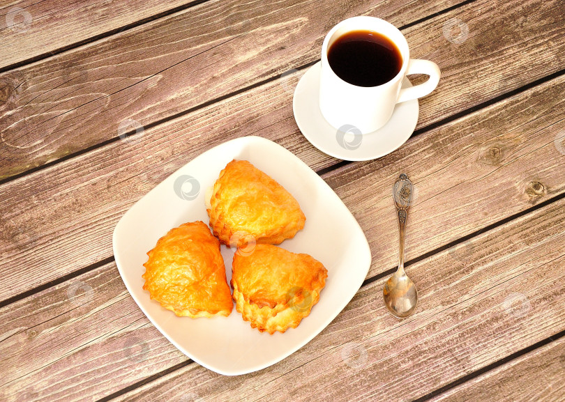 Скачать Тарелка с тремя свежими творожными булочками на деревянном столе, рядом с ней чашка черного кофе и ложка. фотосток Ozero