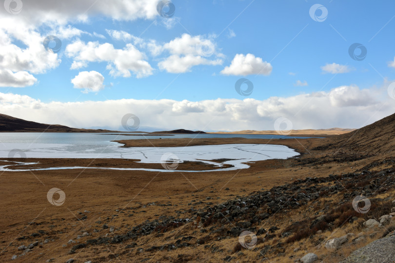 Скачать Красивое огромное озеро, покрытое первым льдом, в долине у подножия пологой горы в солнечный день. фотосток Ozero