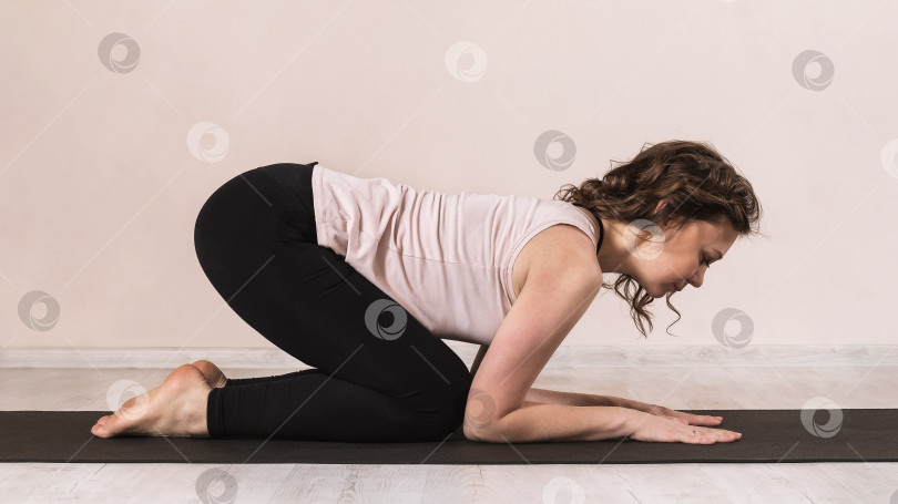 Скачать Женщина в спортивной одежде, практикующая йогу, выполняет упражнение битиласана, поза кошки, на коврике у стены фотосток Ozero