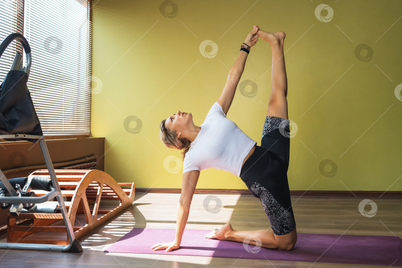 Скачать Женщина, практикующая йогу, выполняет в студии сложную вариацию уштрасаны, позы верблюда фотосток Ozero