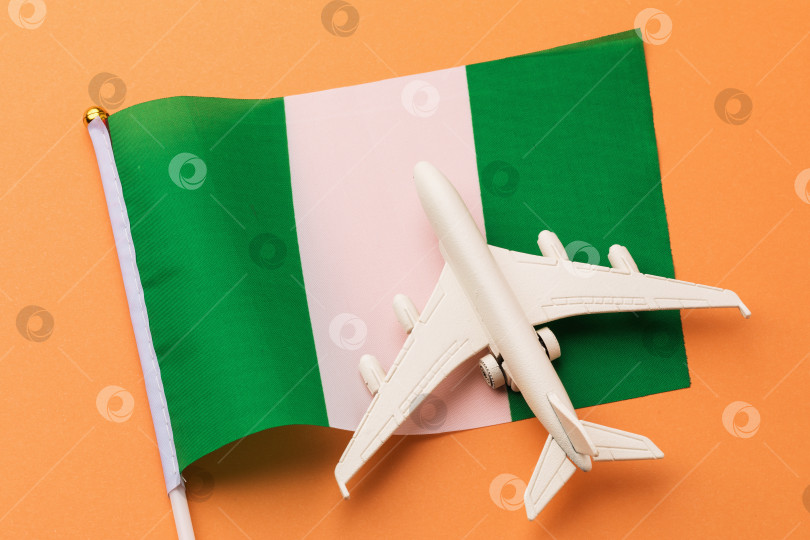 Скачать Нигерийский флаг и игрушечный самолетик на цветном фоне, концепция на тему путешествия в Нигерию фотосток Ozero