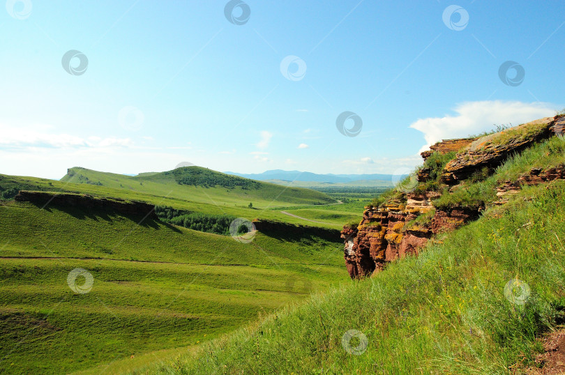 Скачать Скалистые образования из красного песчаника на вершине горы с видом на живописную долину с высокими холмами ясным летним утром. фотосток Ozero