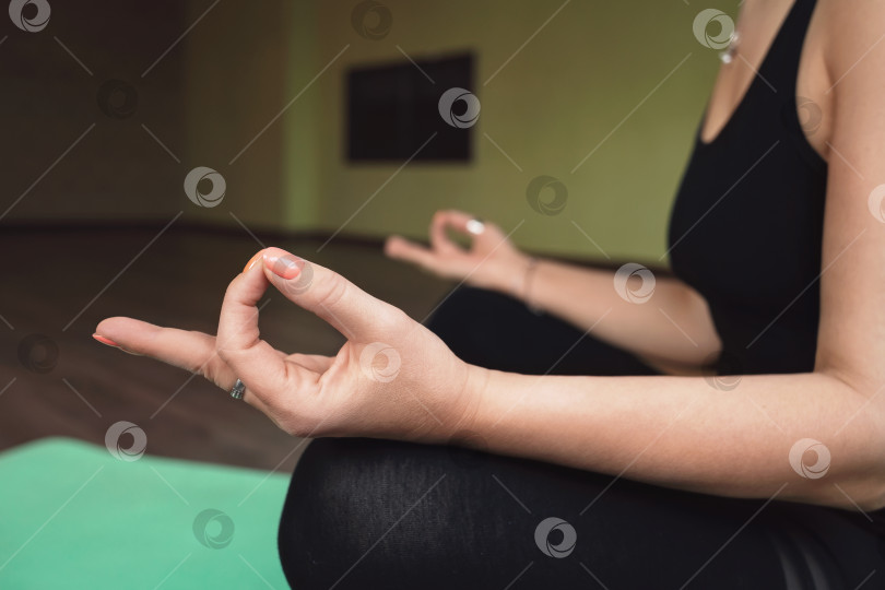 Скачать Женщина, практикующая йогу, занимающаяся медитацией в позе лотоса и выполняющая руками символ джнана мудры, или мудры знания, тренируется в одиночестве в комнате фотосток Ozero