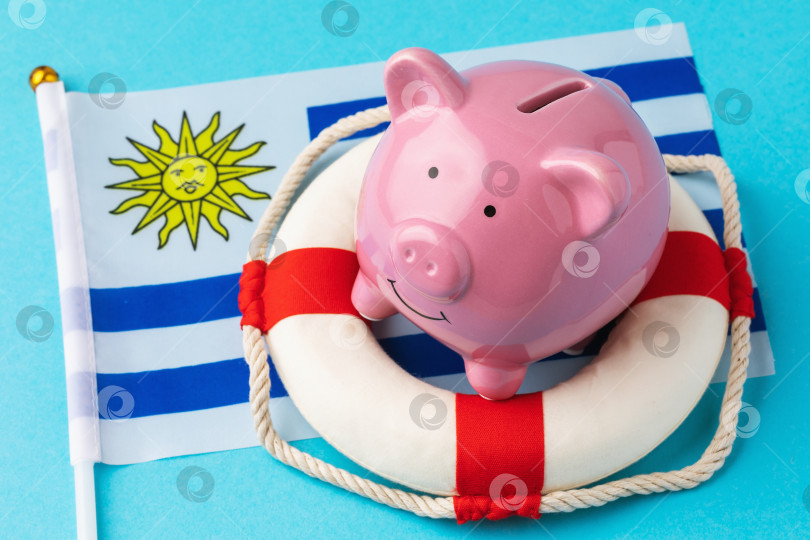 Скачать Копилка, спасательный круг и флаг на синем фоне - концепция спасения уругвайской экономики фотосток Ozero