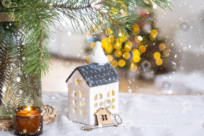 Скачать Ключ и домик небольшого размера в уютном доме с рождественским декором на столе праздничной кухни. Подарок на Новый год. Страхование, переезд в новый дом, ипотека, аренда и покупка недвижимости фотосток Ozero