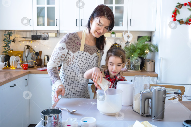 Скачать Мама и дочка на белой кухне готовят печенье, добавляют ингредиенты. Семейный день, подготовка к празднику Рождество, учимся готовить вкусную выпечку, вырезаем фигурки из теста с помощью формочек фотосток Ozero