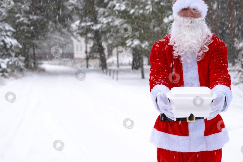 Скачать Контейнеры службы доставки еды в руках Санта-Клауса на открытом воздухе в снегу. Акция в канун Рождества. Готовый горячий заказ, одноразовая пластиковая коробка. Кейтеринг на новогодние праздники. Скопируйте пространство, макетируйте фотосток Ozero