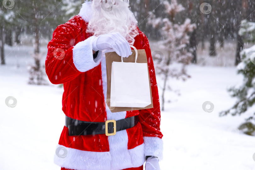 Скачать Санта-Клаус на открытом воздухе зимой и в снегу вручает в руки эко-бумажные пакеты с крафтовым подарком, доставка еды. Покупки, переработка упаковки, ручная работа, доставка на Рождество и Новый год фотосток Ozero