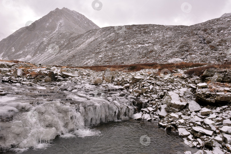 Скачать Река, стекающая с гор, в пасмурный осенний день образует широкую каменную заводь со льдом по краям. фотосток Ozero