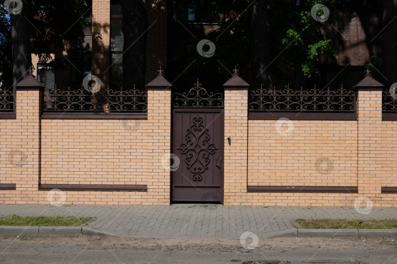 Скачать Светло-коричневый кирпичный забор и кованая железная дверь рядом с дорогой фотосток Ozero