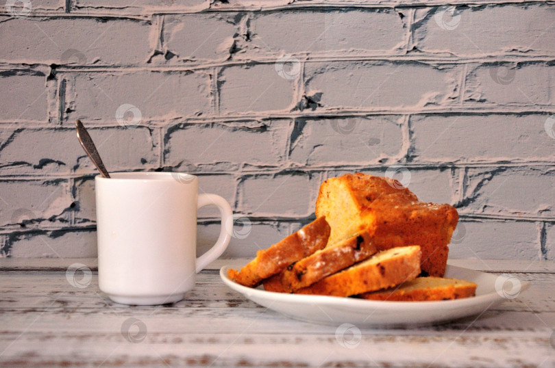 Скачать Тарелка с нарезанным кексом с изюмом и чашка горячего кофе на деревянном столе у кирпичной стены. фотосток Ozero