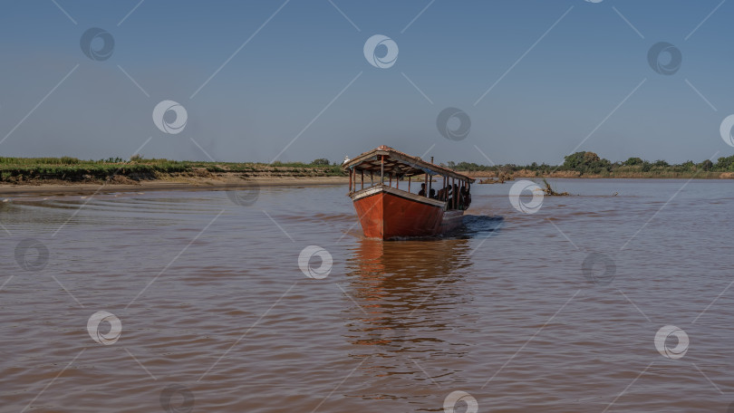 Скачать Лодка с туристами плывет по спокойной реке с красно-коричневой водой. фотосток Ozero