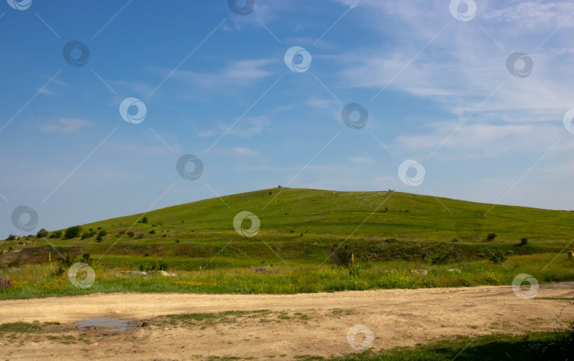 Скачать Зеленый холм и грунтовая дорога на фоне голубого неба с облаками фотосток Ozero