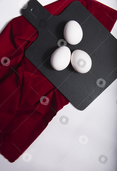Скачать Белые яйца на черной кухонной доске с красной салфеткой фотосток Ozero
