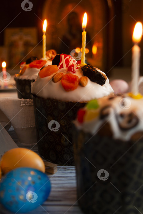 Скачать Пасхальный натюрморт с пасхальным куличом, пасхальными яйцами и горящими свечами в темноте монастырской церкви с русскими иконами на заднем плане, крупным планом фотосток Ozero