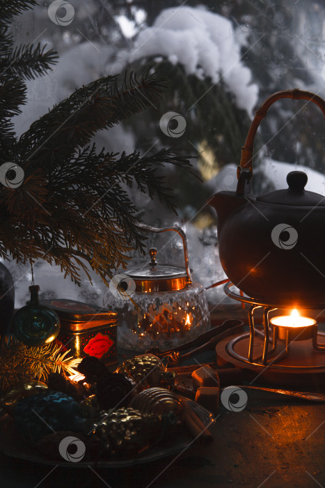 Скачать Зимний натюрморт с чайником и горящими свечами на фоне заснеженного окна фотосток Ozero