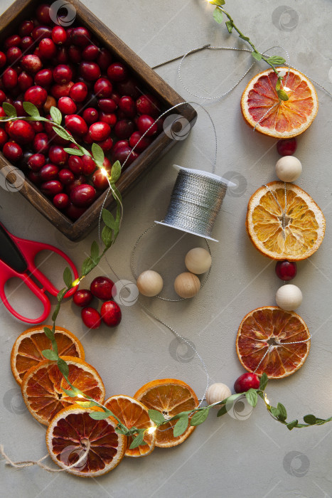 Скачать Домашняя гирлянда из натуральных материалов - сухой апельсиновой стружки, ягод, деревянных шариков, экологически чистая, на деревянном столе с подсветкой. фотосток Ozero