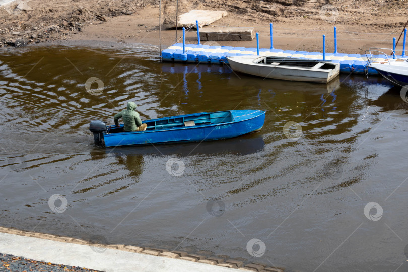 Скачать Рыбак в синей моторной лодке подплывает к пирсу фотосток Ozero