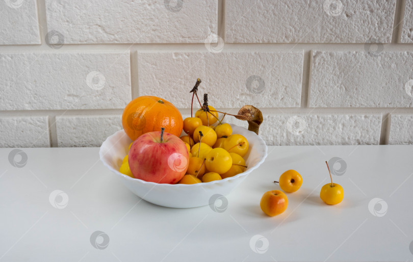 Скачать Мандарин, яблоко и маленькие небесные желтые яблочки на белом блюде фотосток Ozero