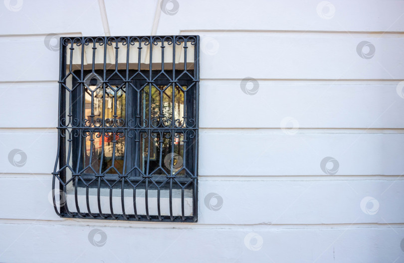 Скачать Одно маленькое закрытое окно, зарешеченное черными металлическими прутьями на белой стене дома фотосток Ozero