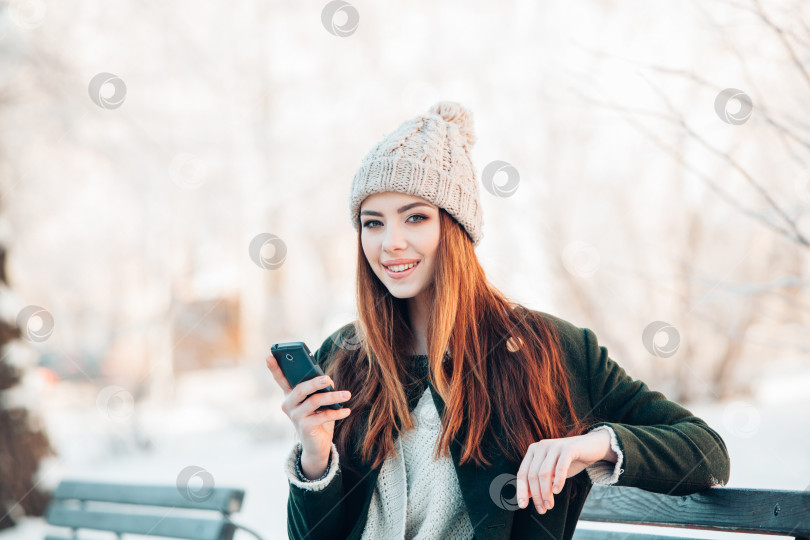 Скачать молодая женщина в зимнем парке разговаривает по мобильному телефону, смс, сидя на скамейке фотосток Ozero