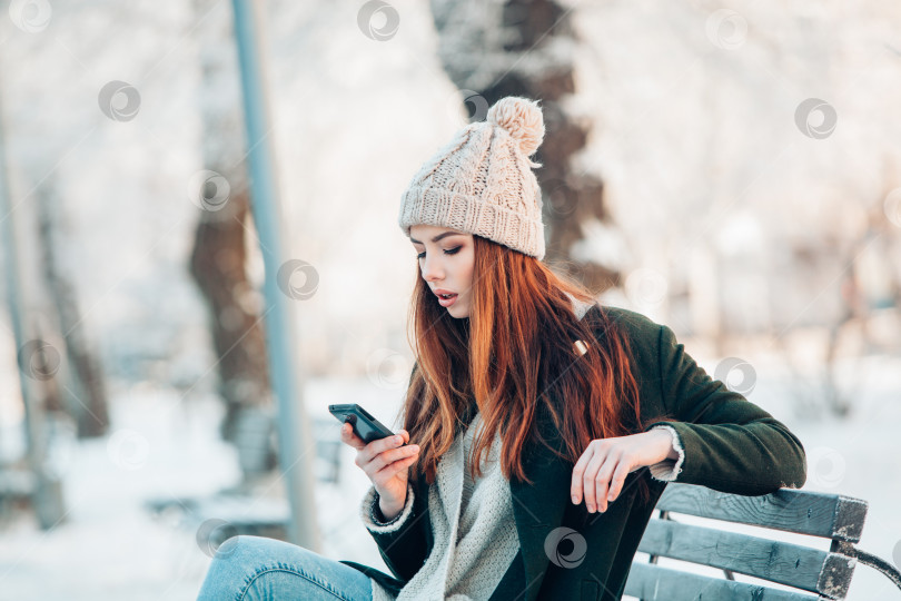 Скачать молодая женщина в зимнем парке разговаривает по мобильному телефону, смс, сидя на скамейке фотосток Ozero