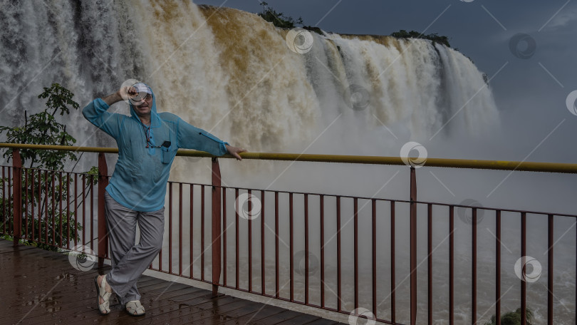 Скачать Мужчина стоит на смотровой площадке у мощного водопада фотосток Ozero