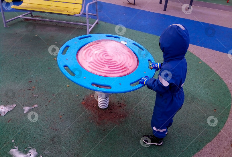 Скачать Ребенок в синем комбинезоне с капюшоном играет на детской площадке фотосток Ozero