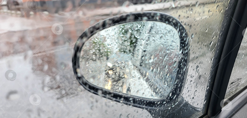 Скачать Вид на боковое стекло автомобиля во время дождя с каплями дождя на нем. Боке на зеркале заднего вида концепт автомобиля, движущегося под дождем фотосток Ozero