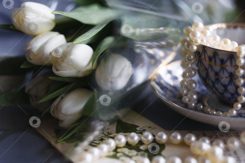 Скачать Белые тюльпаны в бутонах на белом фоне с жемчужными бусинами и чашечкой. Весенняя композиция. фотосток Ozero