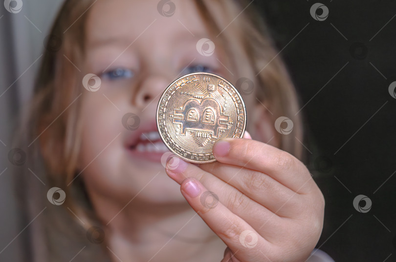 Скачать Маленькая девочка держит в руке монету с символом биткоина фотосток Ozero