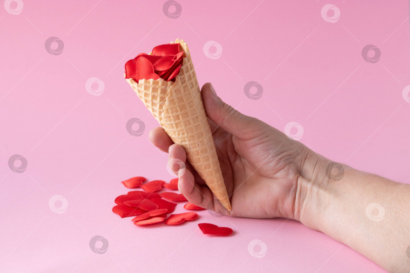 Скачать В руке он держит рожок мороженого с красными сердечками. Креативная фотография пустых вафельных рожков с разбросанными красными сердечками на розовом фоне. Концепция любви, лета, весны фотосток Ozero
