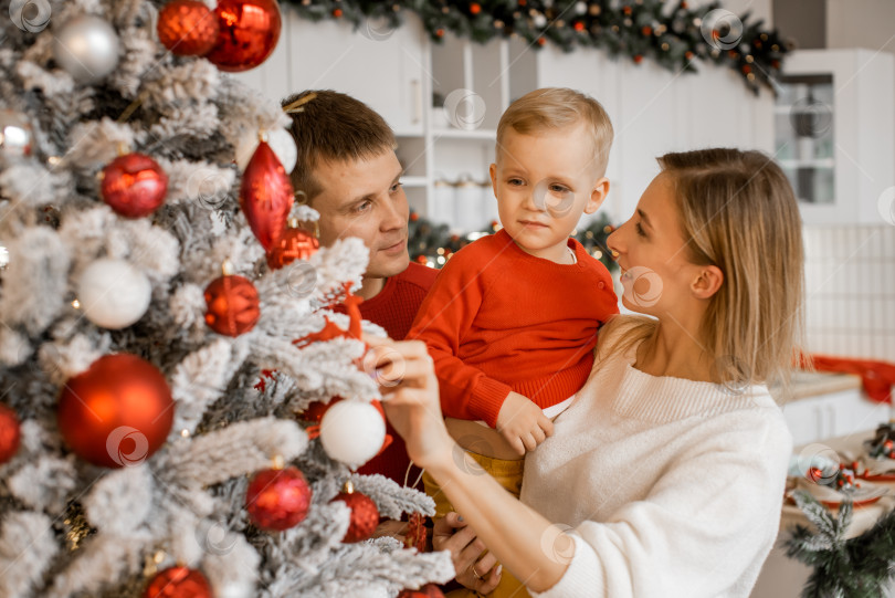 Скачать Счастливая молодая семья наслаждается совместным отдыхом, украшая рождественскую елку фотосток Ozero