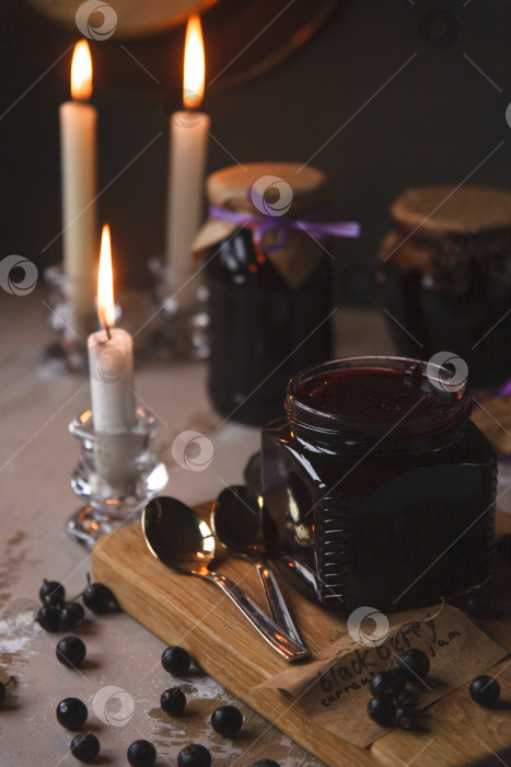 Скачать Стеклянные банки с вареньем из черной смородины в темном винтажном интерьере с горящими свечами фотосток Ozero