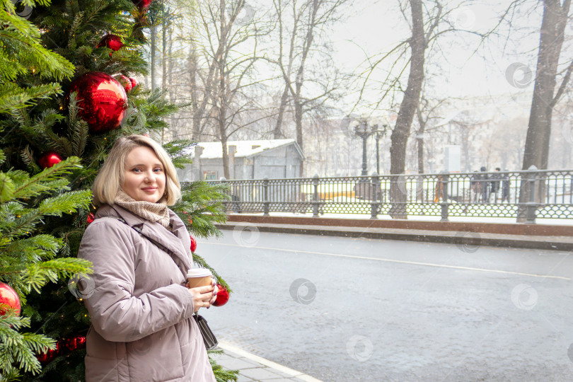 Скачать Женщина в пальто с чашкой кофе у рождественской елки в зимнем городе. Скопировать пробел фотосток Ozero