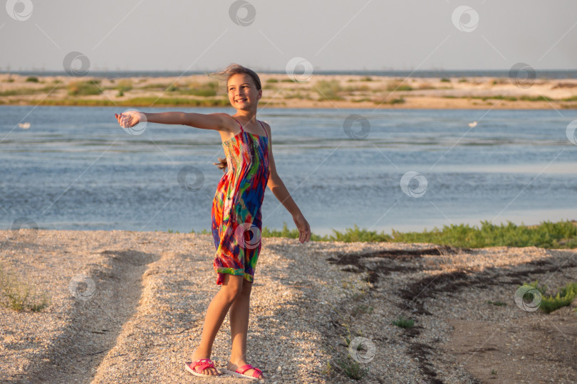 Скачать Красивая девушка, идущая по морскому пляжу, оглядывается по сторонам и протягивает руку. Девушка на берегу лагуны, в ярком летнем платье. Девочка-подросток на пляже с ракушками у моря фотосток Ozero